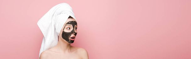plano panorámico de chica impactada con máscara de arcilla facial y toalla en la cabeza mirando hacia otro lado aislado en rosa
 - Foto, Imagen