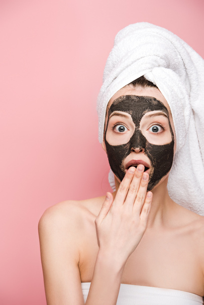 shocked girl with clay mask on face covering mouth with hand and looking at camera isolated on pink - Photo, Image