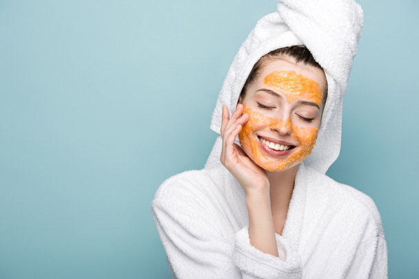 smiling girl with citrus facial mask touching face with closed eyes isolated on blue - Valokuva, kuva