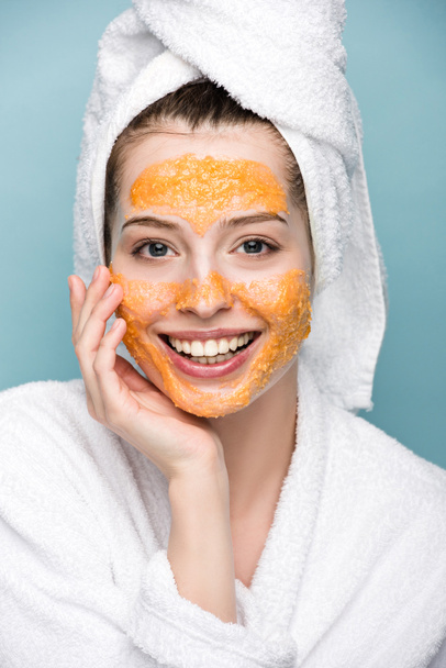 happy girl with citrus facial mask touching face while looking at camera isolated on blue - Φωτογραφία, εικόνα