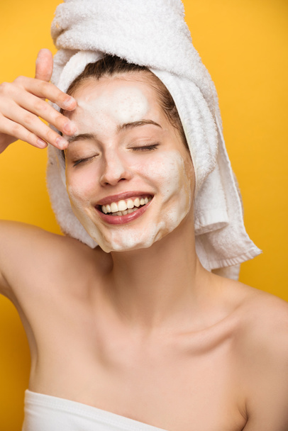 happy girl with moisturizing facial mask touching face with closed eyes on yellow background - Valokuva, kuva