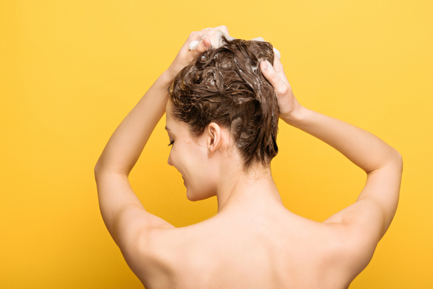 πίσω όψη της γυναίκας πλύσιμο των μαλλιών με σαμπουάν σε κίτρινο φόντο - Φωτογραφία, εικόνα