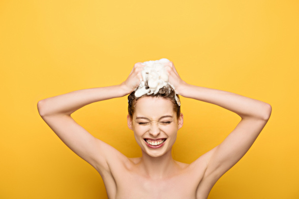 wesoła dziewczyna uśmiecha się z zamkniętymi oczami podczas mycia włosów na żółtym tle - Zdjęcie, obraz