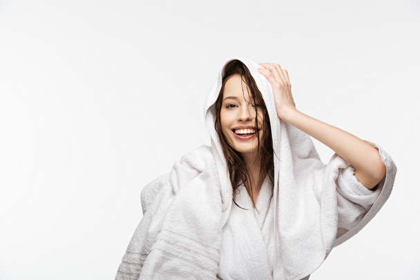 alegre chica limpiando húmedo cabello limpio con toalla blanca mientras mira la cámara aislada en blanco
 - Foto, Imagen