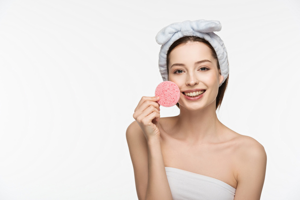 happy girl holding cosmetic sponge near face while looking at camera isolated on white - Photo, Image