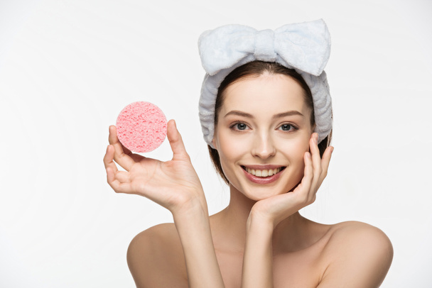 glückliches Mädchen zeigt kosmetischen Schwamm und berührendes Gesicht isoliert auf weiß - Foto, Bild