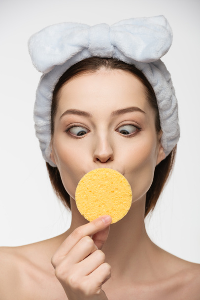 mujer joven entrecerrando los ojos mientras mira esponja cosmética aislada en blanco
 - Foto, imagen