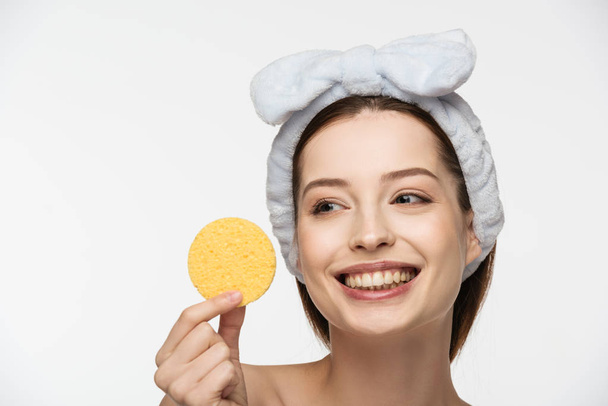 feliz jovem mulher olhando para esponja cosmética isolada no branco
 - Foto, Imagem