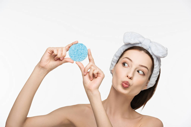 aantrekkelijk meisje met eend gezicht expressie kijken naar cosmetische spons geïsoleerd op wit - Foto, afbeelding