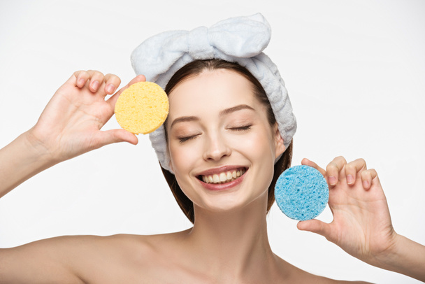 vrolijk meisje met gesloten ogen houden kleurrijke cosmetische sponzen geïsoleerd op wit - Foto, afbeelding