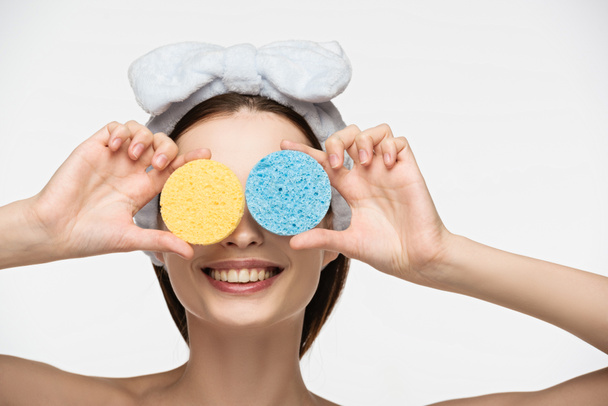 smiling girl covering eyes with colorful cosmetic sponges isolated on white - Foto, afbeelding