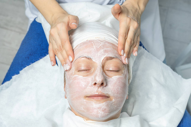 Close-up schoonheidsspecialiste handen maken anti-leeftijd procedures, gezicht en hoofd massage voor vrouwelijke klant op middelbare leeftijd in schoonheidskliniek. Cosmetoloog doet huidverzorging .Gezondheidszorg therapie - Foto, afbeelding