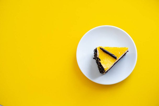 Slice of chocolate cake with orange jelly top on flat yellow background - Foto, afbeelding