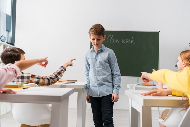 selective focus of classmates pointing with fingers at frustrated schoolboy covering face, bullying concept  - Fotoğraf, Görsel