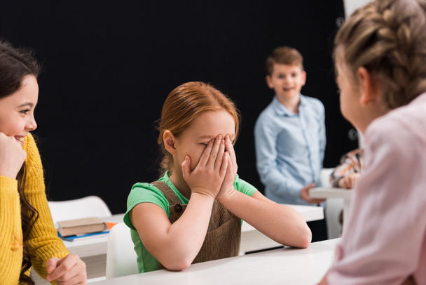 selective focus of upset kid crying near classmates on black, bullying concept  - Foto, Imagen