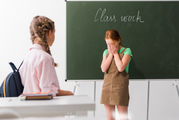 selectieve focus van schoolkind dekking gezicht terwijl huilen in de buurt van klasgenoot, pesten concept  - Foto, afbeelding