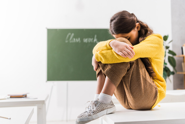 bullied schoolgirl covering face while crying in classroom  - Foto, Imagen
