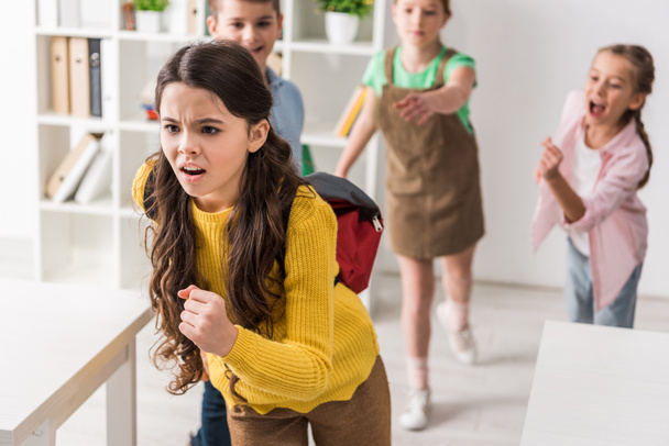 selective focus of bullied schoolgirl running from cruel classmates, bullying concept - Photo, Image