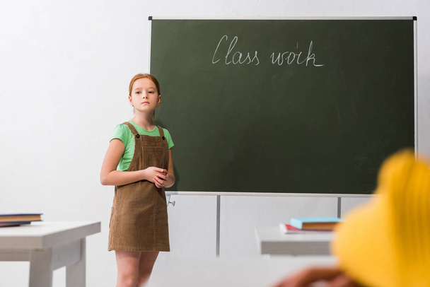 Selektiver Fokus einer aufgebrachten Schülerin, die neben einer Tafel mit Klassenarbeiten-Schriftzug steht  - Foto, Bild