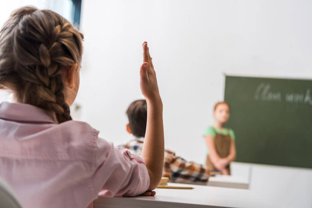 selective focus of schoolgirl with raised hand near classmates  - Fotografie, Obrázek