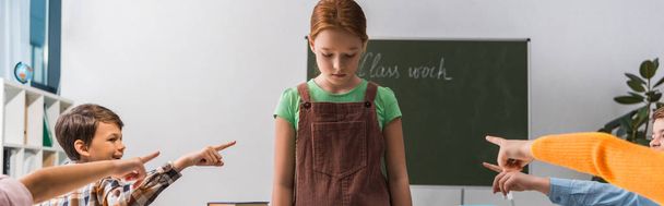 panoráma felvétel kegyetlen osztálytársak ujjal mutogatva depressziós bántalmazott iskolás lány az osztályteremben  - Fotó, kép