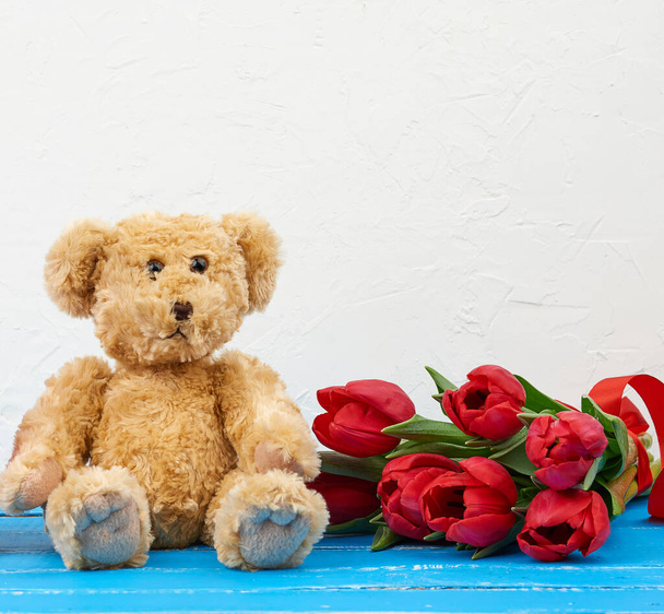 cute brown teddy bear sits on a blue wooden background and bouqu - Φωτογραφία, εικόνα