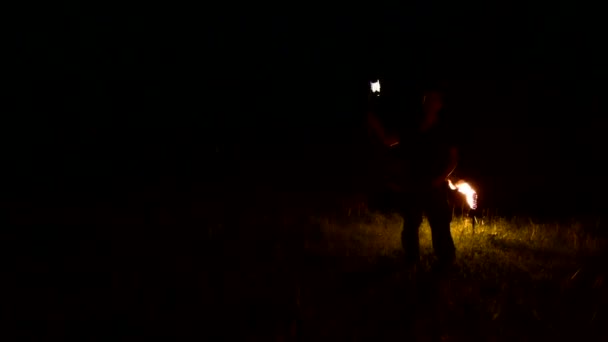 Zbliżenie. Młody mężczyzna w ciemności przedstawia obracające się płonące kulki poi. Pokaz ognia - Materiał filmowy, wideo