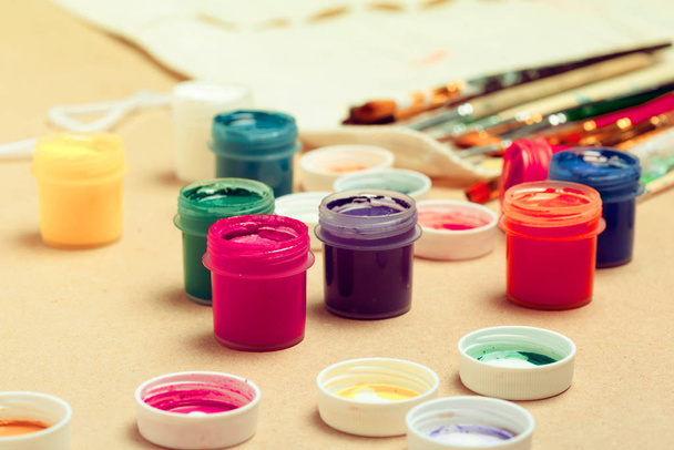 Jars with colorful gouache and brush on beige background close up. Creative Photo - Foto, Imagen