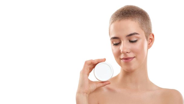 Testing daily cream. Young attractive blonde woman with short haircut demonstrating cosmetic product while standing in studio against white background - Foto, imagen