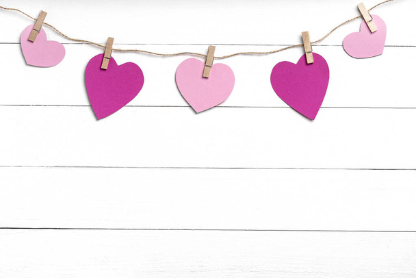 Прищіпки з рожевими серцями, що звисають на мотузці за білою дерев'яною поверхнею
. - Фото, зображення