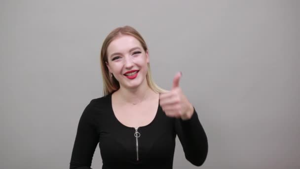 Молода блондинка в чорній куртці щаслива жінка показує її великий палець
 - Кадри, відео