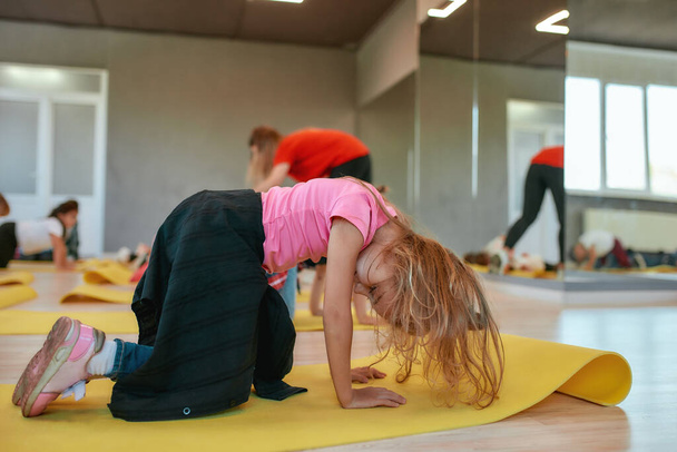 Παιδιά και σπορ. Πλάγια άποψη ενός μικρού κοριτσιού που κάνει γυμναστικές ασκήσεις με γυναίκα γυμνάστρια στο στούντιο χορού. Παιδιά που τεντώνονται σε στρώματα γιόγκα - Φωτογραφία, εικόνα