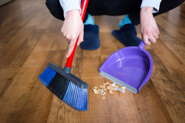 Woman in blue slippers using indoor broom for floor cleaning, collecting dirt. - Fotografie, Obrázek