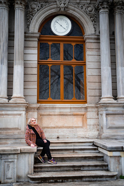 A blonde girl sits on the steps of an old building in the rain and smiles - Foto, Imagen