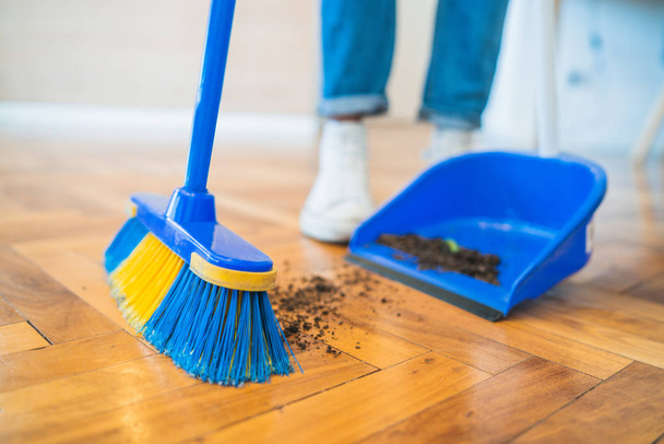 Latin man sweeping wooden floor with broom at home. - 写真・画像