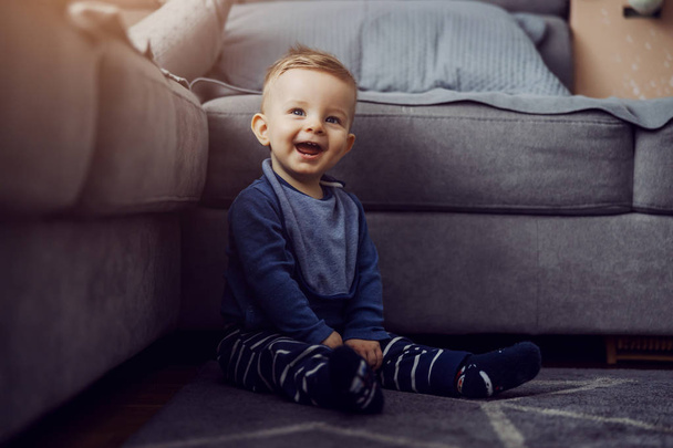 Adorable laughing blond little baby boy sitting on floor and looking up. - Fotó, kép