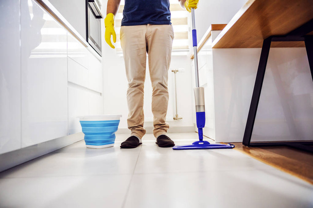 Nuori tyytyväinen mies seisoo keittiössä moppi kädessä. Keittiön lattia on puhdas
. - Valokuva, kuva