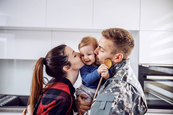 Jonge soldaat is thuisgekomen en hij is gelukkig met zijn familie. man en vrouw zoenen hun geliefde enige zoon. - Foto, afbeelding