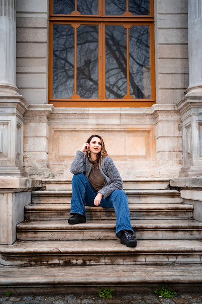 Red haired beautiful girl sitting on the steps of an old building in the rain - Foto, Bild