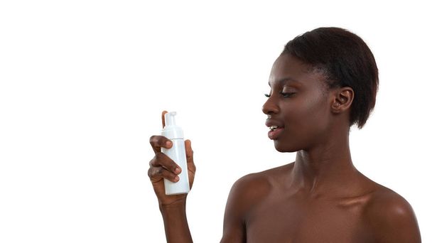 Making her skin clean and fresh. Portrait of beautiful young african woman demonstrating cosmetic product and looking at camera while standing in studio against white background - Foto, Bild