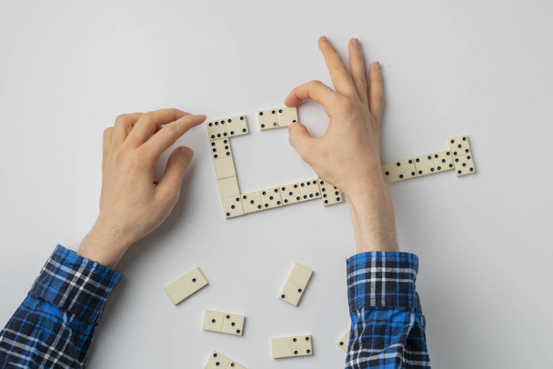 a close up person hand holding domino pieces and play the game on the white table - Foto, imagen