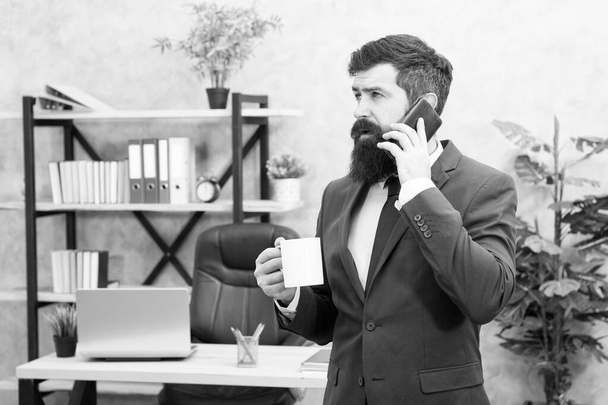 Man bearded businessman hold cup and smartphone. Coffee is pledge of successful negotiations. Caffeine addicted. Mobile call. Start day with coffee. Coffee relaxing break. Boss enjoying energy drink - Φωτογραφία, εικόνα