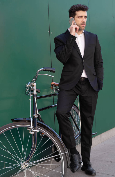 Человек в костюме и на классическом велосипеде говорит по телефону
 - Фото, изображение