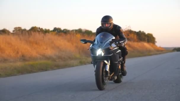 秋の田舎道でオートバイレースをしています。高速道路で現代のスポーツバイクに乗ってヘルメットで若い男。旅行中にバイクを運転する男。自由の概念。フロントビューを閉じる - 映像、動画