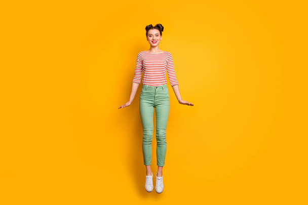 Full length photo of attractive pretty lady jumping high up rejoicing traveler abroad wear red white pullover shirt green pants footwear isolated bright yellow background - Photo, Image