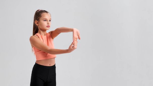 Everyone in life needs balance. Flexible cute little girl child looking aside while stretching her hands isolated on a white background. Sport, fitness, active lifestyle concept. Horizontal shot. - Fotó, kép