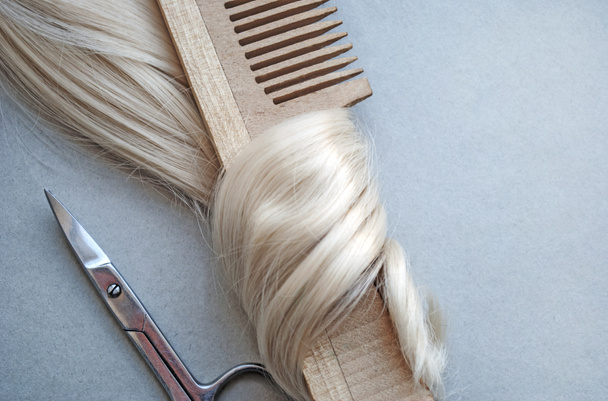Top view of a wooden comb in curls of delicate blond blonde hair and scissors. On a delicate beige, gray background. The concept of a beauty salon, hairdresser. Blank for design. - Photo, Image