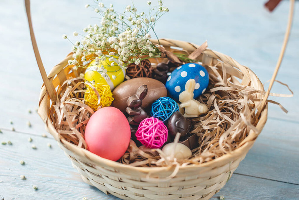 Cesto regalo di Pasqua con cioccolato a forma di uova e conigli e uova luminose con un bouquet primaverile di fiori
 - Foto, immagini