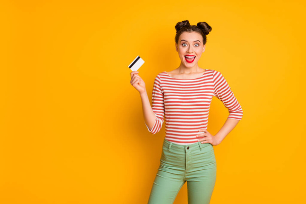 Photo of pretty excited funny lady open mouth holding credit card wireless online money wear striped red white shirt green pants isolated bright yellow color background - Фото, изображение