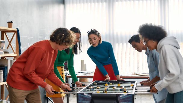 Playing game with coworkers. Young and happy multicultural people in casual wear playing table soccer in the modern office. Office activities. Having fun together. Happy employees - 写真・画像